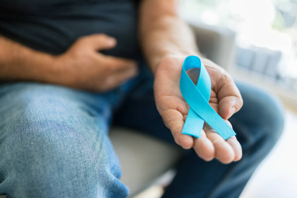 Elinde mavi bir kanser farkındalığı kurdelesi tutan kıdemli bir adam. - Fotoğraf, Görsel