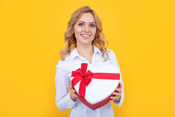 女性の笑顔は黄色の背景にプレゼントハートボックスを保持します. - 写真・画像