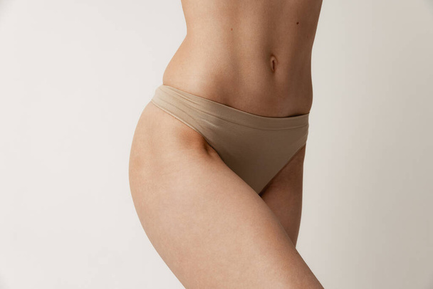 Sportive muscular female body, buttocks in beige underwear posing isolated over grey studio background. Slim belly. Concept of beauty, body and skin care, health, plastic surgery, cosmetics, spa. - Zdjęcie, obraz