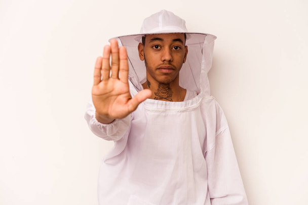 Jonge Afro-Amerikaanse imker geïsoleerd op witte achtergrond staande met uitgestrekte hand met stopteken, voorkomen dat u. - Foto, afbeelding