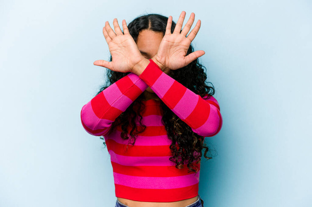 Nuori latino nainen eristetty sinisellä taustalla pitää kaksi kättä ristissä, kieltäminen käsite. - Valokuva, kuva