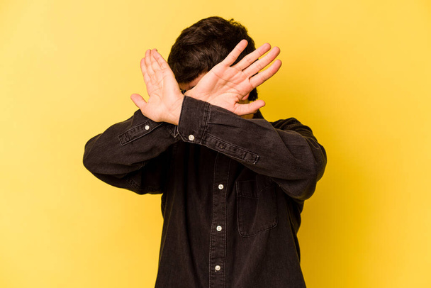 Young caucasian man isolated on yellow background keeping two arms crossed, denial concept. - Fotó, kép