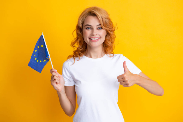 Πορτρέτο της φιλικής όμορφης γυναίκας που κρατά τη σημαία της Ευρωπαϊκής Ένωσης, σύμβολο της Ευρώπης, σύνδεσης και της κοινότητας της ΕΕ. Στούντιο απομονωμένο κίτρινο φόντο - Φωτογραφία, εικόνα