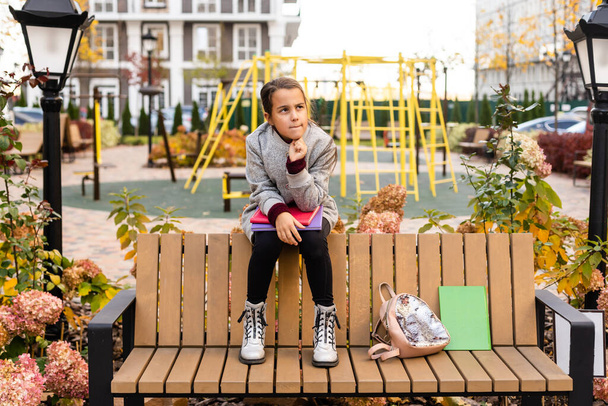 Μαθητρια, διαβάζοντας το βιβλίο ενώ κάθονται στον πάγκο στο πάρκο. - Φωτογραφία, εικόνα