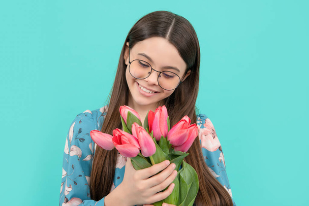 bambino felice in occhiali con tulipani. giorno delle madri o delle donne. il bambino tiene fiori per 8 di marzo. teen girl con bouquet primavera su sfondo blu. floreale presente. - Foto, immagini