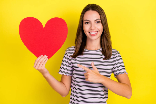 Photo of sweet millennial brunette lady point heart wear white t-shirt isolated on yellow background. - Foto, immagini