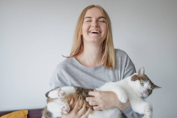 Retrato de la joven rubia feliz mujer de 30 años sosteniendo lindo gato tabby con ojos verdes. Hembra abrazando gato en manos - Foto, imagen