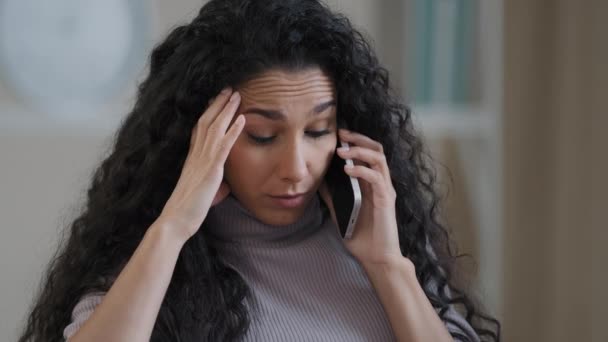 Ανήσυχη αραβική ισπανόφωνη γυναίκα νεαρή κοπέλα φοιτητής επιχειρηματίας μιλάμε κινητό τηλέφωνο κάθονται στο σπίτι απογοητευμένη γυναίκα ελεύθερος επαγγελματίας λαμβάνουν άσχημα νέα πρόβλημα παρεξήγηση έχει πονοκέφαλο αρνητικό συναίσθημα - Πλάνα, βίντεο