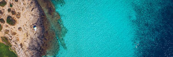 Begrip zomervakantie. Uitzicht van boven, adembenemend uitzicht op een geweldig strand met parasols en turquoise helder water. Bovenaanzicht op een ligstoel onder een parasol op het zandstrand - Foto, afbeelding