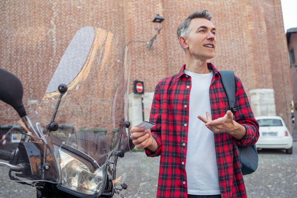 In the street. Man in a plaid red shirt standing near the street motobike - Foto, Imagen