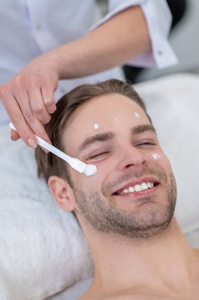 Moisturizing procedure. Cosmetologist applying moisturizing cream on clients face - 写真・画像