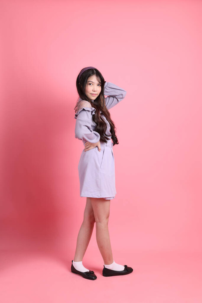 A jovem mulher asiática bonito com preppy vestido de pé sobre o fundo rosa. - Foto, Imagem