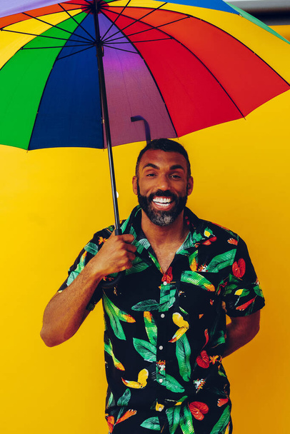 handsome african american man in hawaian shirt posing with colorful umbrella  - Фото, изображение