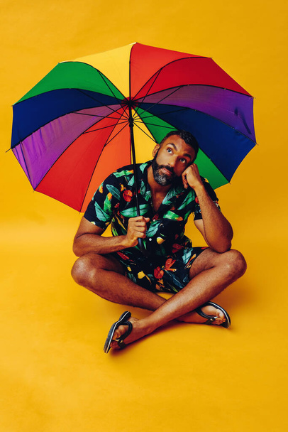 knappe Afrikaanse Amerikaanse man poseren met kleurrijke paraplu op gele achtergrond - Foto, afbeelding