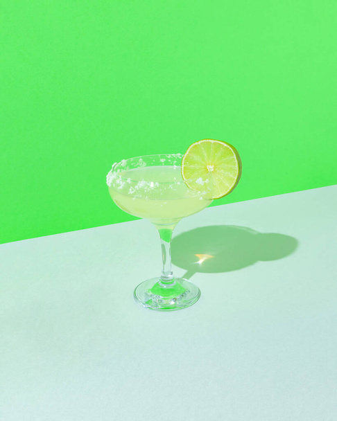 Composition minimale avec verre à cocktail et lime fraîche tranchée sur fond vert géométrique. Idée de rafraîchissement tropical avec espace de copie. - Photo, image