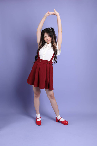 Милая молодая азиатка с красивой одеждой, стоящая на фиолетовом фоне. - Фото, изображение
