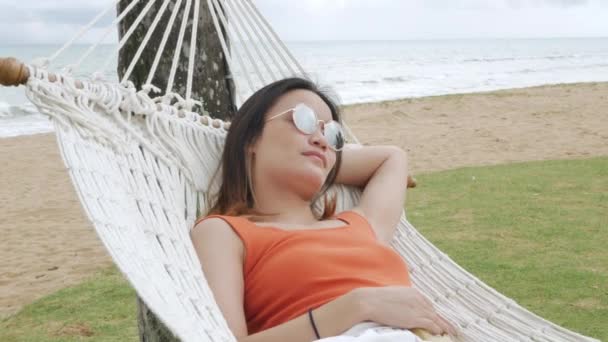 Asijská žena relaxační a na houpací síti v blízkosti pláže pod kokosovým stromem v době dovolené - Záběry, video