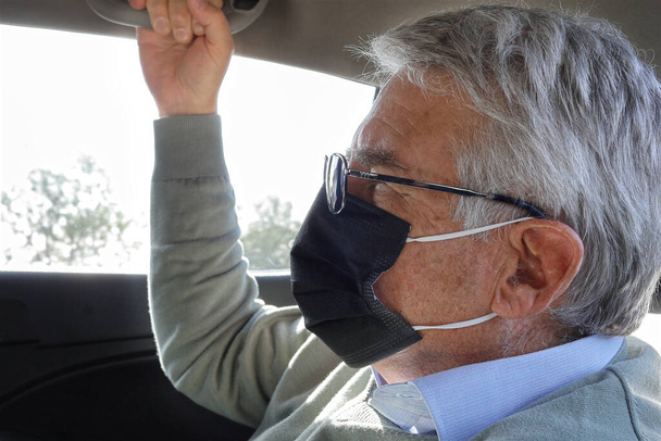 boční pohled senior muž sedí na zadním sedadle auta s objektivem a maskou - Fotografie, Obrázek