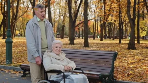 Літня кавказька безтурботна пара середнього віку і бабуся і дідусь ходять в осінньому парку дідусь штовхають старшу зрілу жінку з хворобою в інвалідному візку заміжні партнери проводять час разом
 - Кадри, відео
