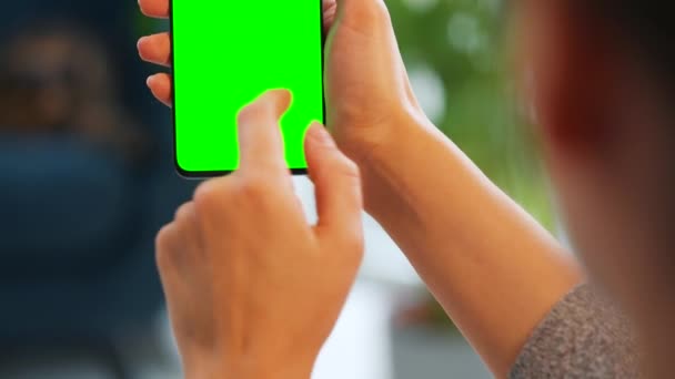 垂直モードで緑のモックアップ画面とスマートフォンを使用して自宅で女性。女の子はインターネットを閲覧し、コンテンツ、ビデオ、ブログを見る. - 映像、動画