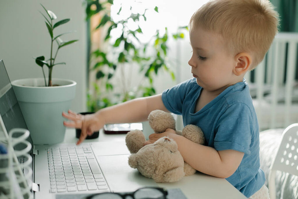 Маленький симпатичный мальчик, использующий ноутбук в спальне дома. Семейный образ жизни - Фото, изображение