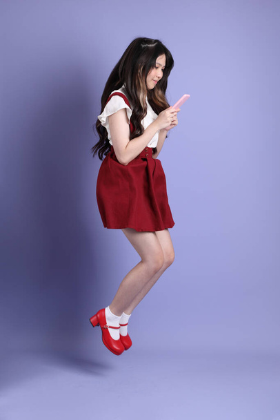 Милая молодая азиатка с красивой одеждой, стоящая на фиолетовом фоне. - Фото, изображение