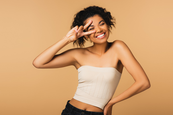 cheerful african american woman with bare shoulders showing peace sign isolated on beige  - Foto, immagini