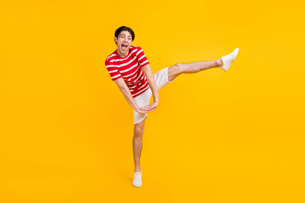 Full size photo of happy positive young man hold hands raise leg funky mood isolated on yellow color background. - Foto, Imagem