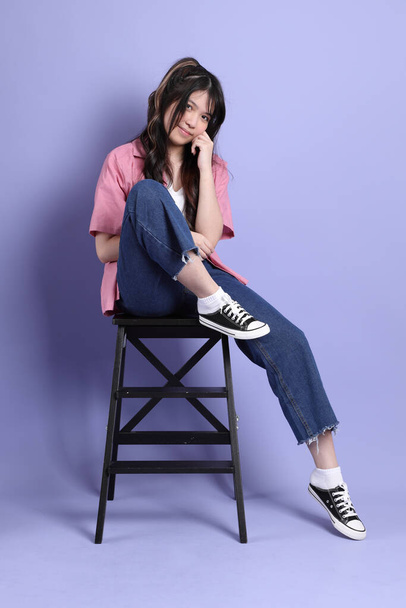 The cute young Asian girl with casual clothes sitting on the purple background. - Foto, Imagen