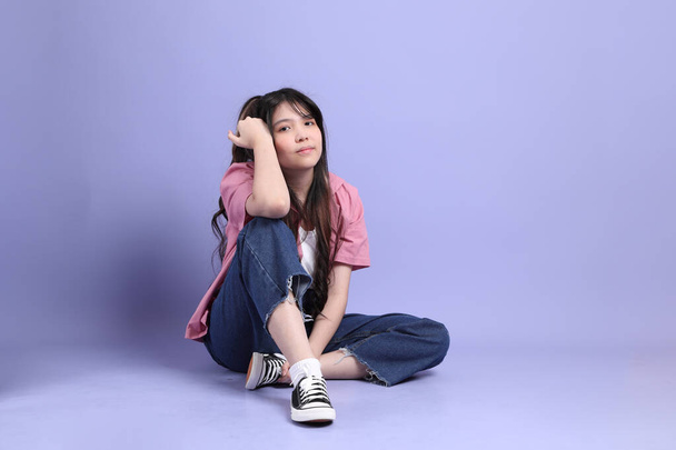 Az aranyos fiatal ázsiai lány alkalmi ruhák áll a lila háttér. - Fotó, kép