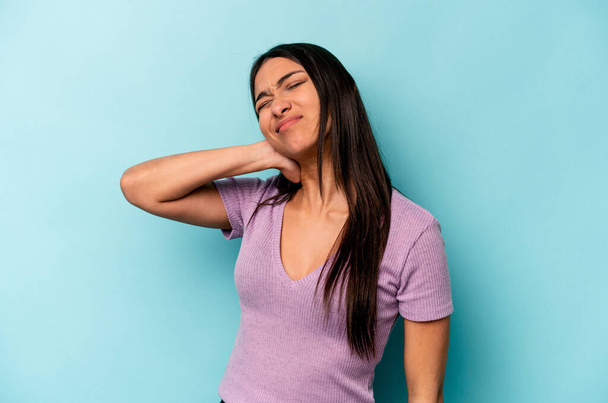Nuori latino nainen eristetty sinisellä pohjalla, jolla on niskakipu stressin vuoksi, hieromalla ja koskettamalla sitä käsin. - Valokuva, kuva