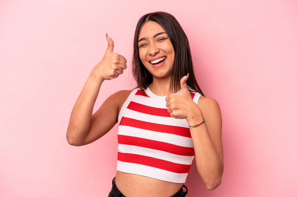 Nuori latino nainen eristetty vaaleanpunainen tausta nostaa molemmat peukalot ylös, hymyillen ja luottavainen. - Valokuva, kuva