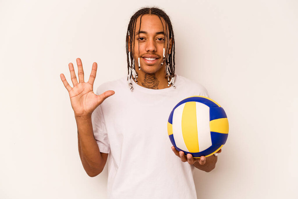 Jeune homme afro-américain jouant au volley isolé sur fond blanc souriant gai montrant numéro cinq avec les doigts. - Photo, image