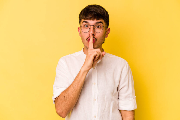 Young caucasian man isolated on yellow background keeping a secret or asking for silence. - Foto, Imagen