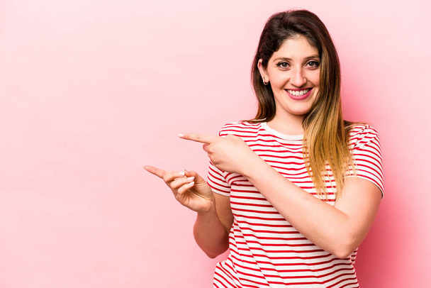 Young caucasian woman isolated on pink background excited pointing with forefingers away. - Photo, Image
