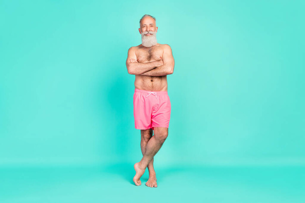 Photo of cheerful positive bearded old man folded hands wear pink shorts isolated turquoise color background. - Foto, Bild