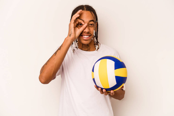 Jeune homme afro-américain jouant au volley isolé sur fond blanc excité en gardant ok geste sur oeil. - Photo, image