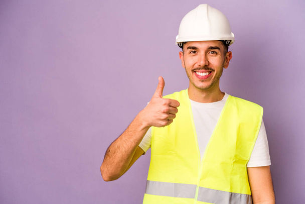 Mladý hispánský dělník muž izolovaný na fialovém pozadí s úsměvem a zvednutím palce nahoru - Fotografie, Obrázek