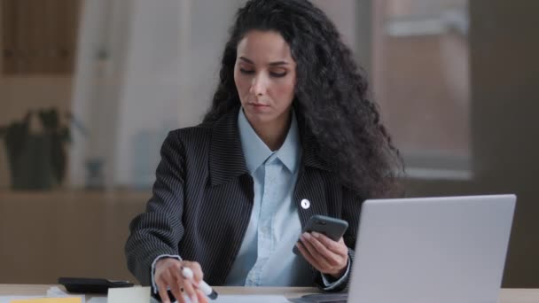 Fókuszált arab spanyol hispán fiatal üzletasszony multitasking specialista női könyvvizsgáló írni feladatokat ragacsos jegyzetek kezelése papírmunka szervezése marketing terv használata mobil eszköz mobiltelefon keresési információk - Felvétel, videó