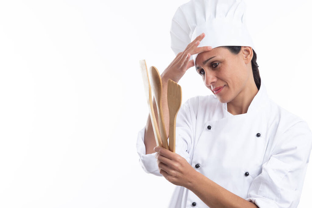 Giovane giovane caucasico interessato chef in abito da chef mentre tiene gli strumenti da cucina isolati su sfondo bianco con spazio copia. - Foto, immagini