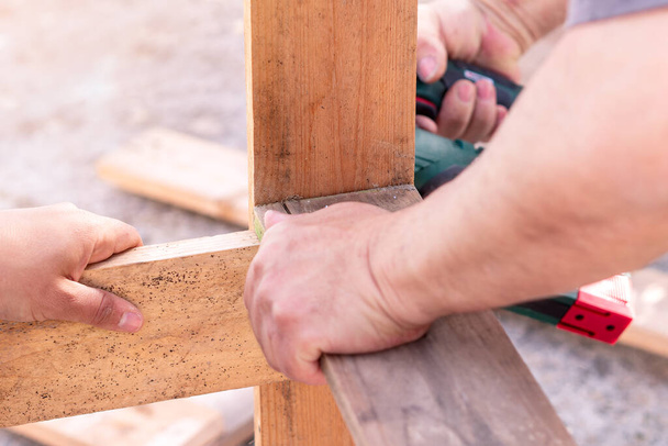 Close-up of two men nailing wooden planks with a nail gun. Selective focus. - Photo, Image