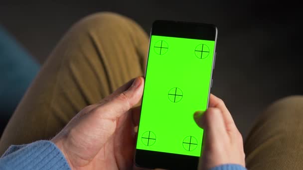 Hombre usando smartphone con pantalla de maqueta verde en modo vertical. Hombre navegando por Internet, viendo contenido, videos, blogs. - Imágenes, Vídeo