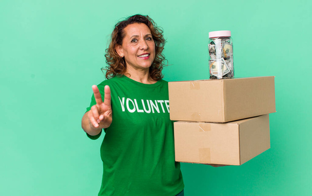 middle age woman smiling and looking happy, gesturing victory or peace. volunteer and donation concept - Photo, Image