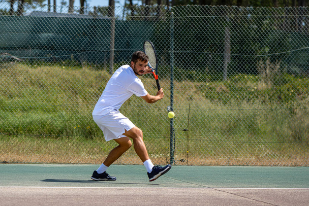 Tennis player hitting backhand at ball with racket on court. - Foto, Imagen