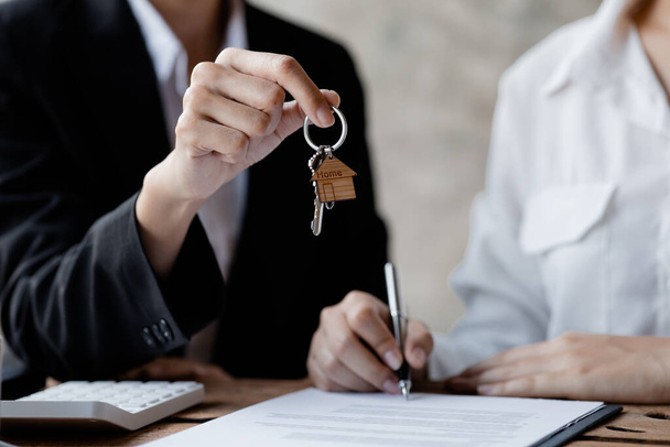 A home rental company employee is handing the house keys to a customer who has agreed to sign a rental contract, explaining the details and terms of the rental. Home and real estate rental ideas. - Photo, Image