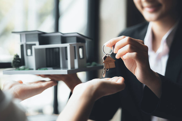 A home rental company employee is handing the house keys to a customer who has agreed to sign a rental contract, explaining the details and terms of the rental. Home and real estate rental ideas. - Zdjęcie, obraz