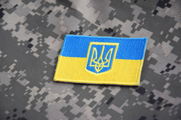 Ουκρανική σημαία με το οικόσημο στο φόντο του στρατιωτικού καμουφλάζ. Πόλεμος στην Ουκρανία. Σταματήστε τον πόλεμο.. - Φωτογραφία, εικόνα