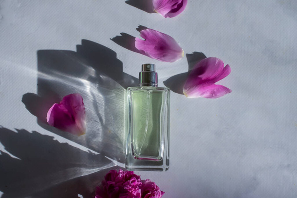 Parfumflesje, pioenbloem op een lichte ondergrond - Foto, afbeelding