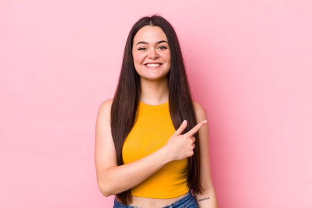 young adult woman smiling cheerfully, feeling happy and pointing to the side and upwards, showing object in copy space - Photo, Image