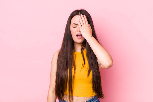 young adult woman looking sleepy, bored and yawning, with a headache and one hand covering half the face - Foto, afbeelding